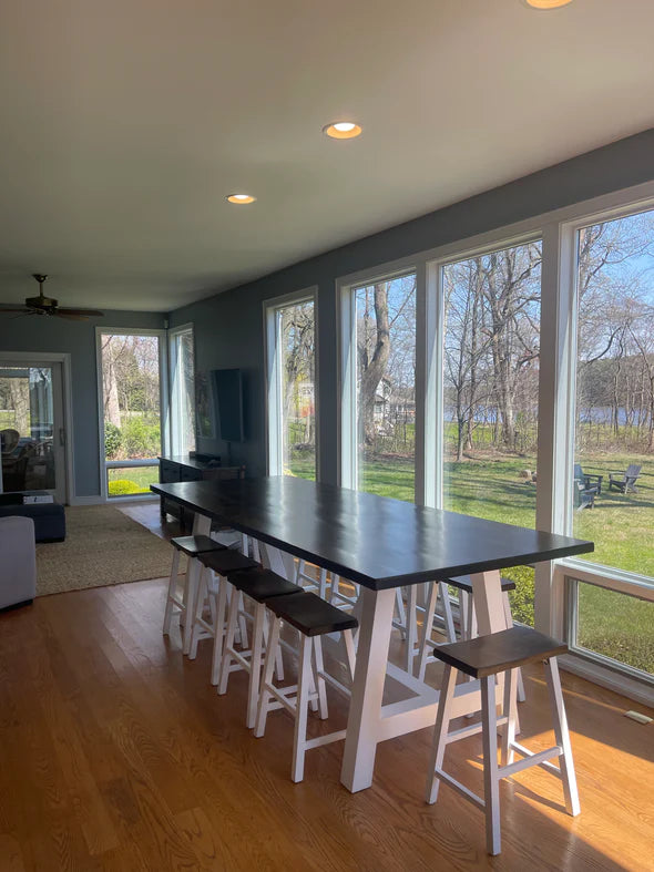 hardwood dining table dark top white base 10 matching stools on light hardwood floor with large windows behind